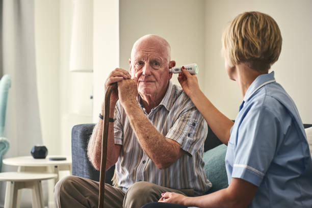 Healthcare worker checking senior man's temperature while sitting on sofa at care home