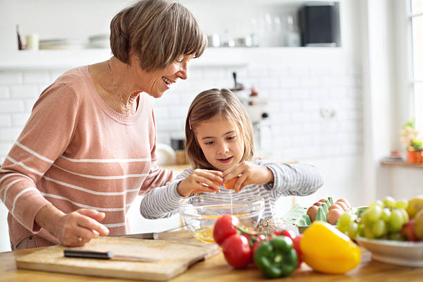 Happy grandmother teaching little girl how to cook eggs